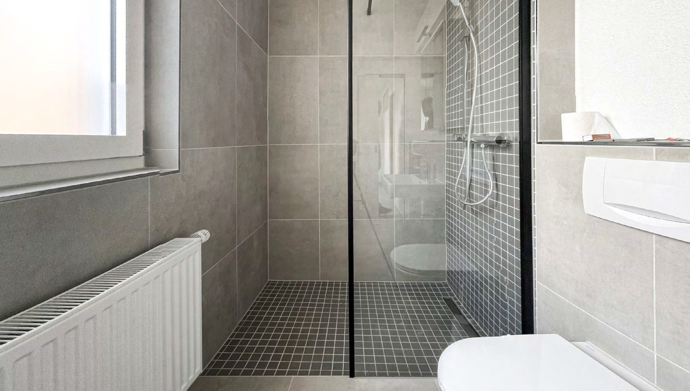 Bodengleiche Glasdusche mit grauem Mosaikboden und grossformatigen Wandfliesen